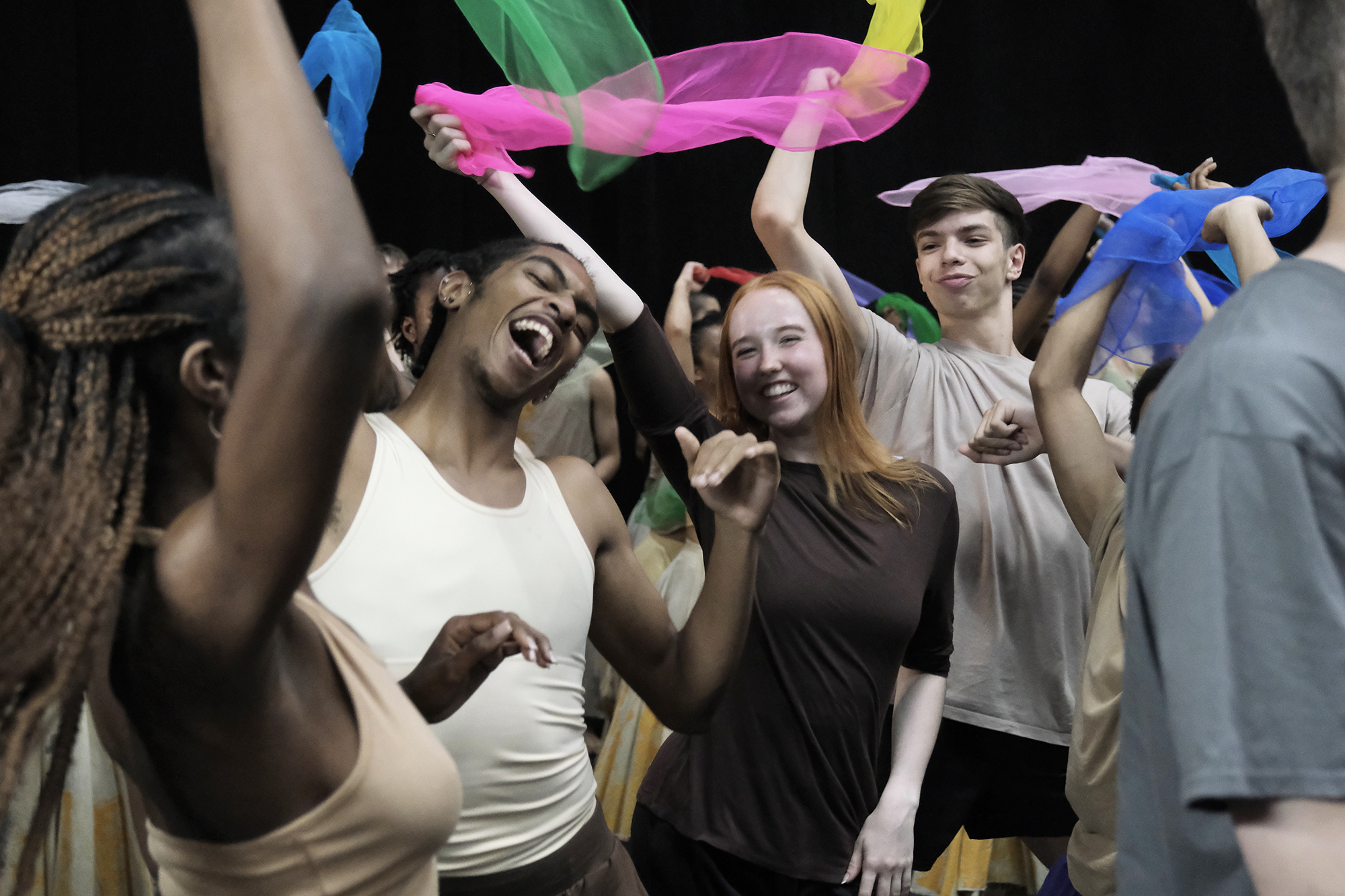 young people mixed genders and races dancing together with big smiling faced waving brightly colour scarfs. 